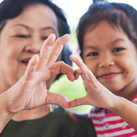Mother and daughter out of focus in background with hands in foreground making heart shape